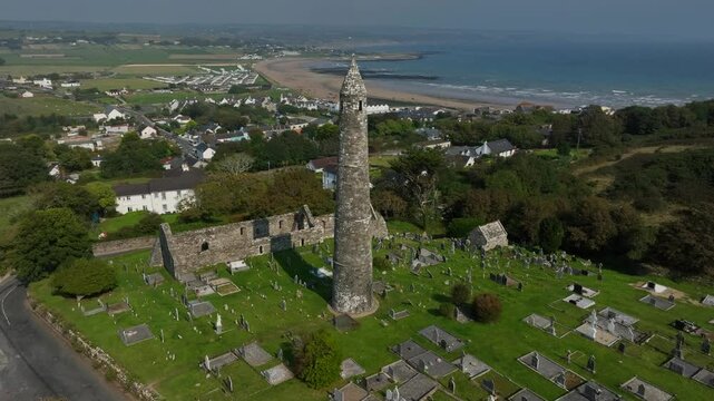 St. Declan's Monastery, Ardmore, County Waterford, Ireland, September 2024. Drone orbits clockwise around the Round Tower with coastal panoramic views of the 12th century graveyard and Cathedral ruin.