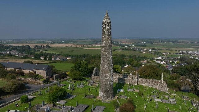 St. Declan's Monastery, Ardmore, County Waterford, Ireland, September 2024. Drone orbits clockwise around weathered Round Tower with sweeping coastal views of the beach from the grassy hillside.