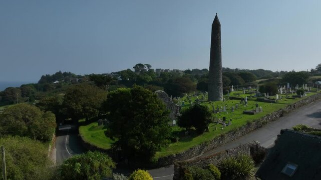 St. Declan's Monastery, Ardmore, County Waterford, Ireland, September 2024. Drone orbits clockwise above the trees by the bend in the road around Cathedral and Round Tower in middle of the cemetery.