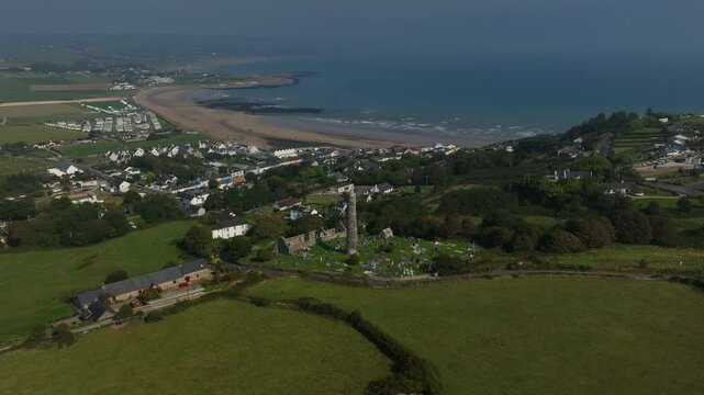 St. Declan's Monastery, Ardmore, County Waterford, Ireland, September 2024. Drone ascends in a panoramic counter clockwise orbit high above Round Tower and graveyard as a road winds toward the coast.
