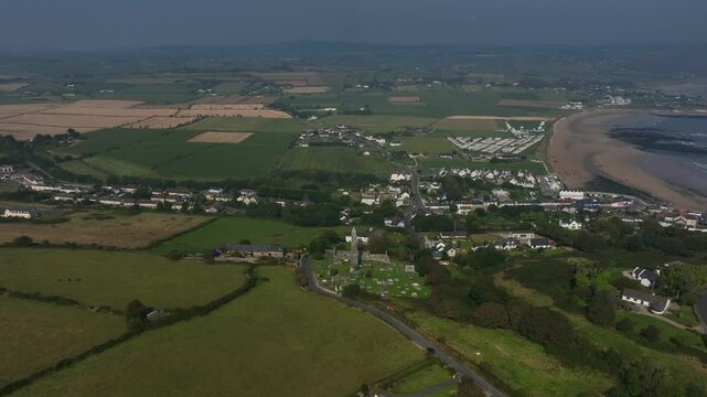 St. Declan's Monastery, Ardmore, County Waterford, Ireland, September 2024. Drone panoramic high angle orbit clockwise around Round Tower with farmland, beach and ocean waves crashing on the coast.