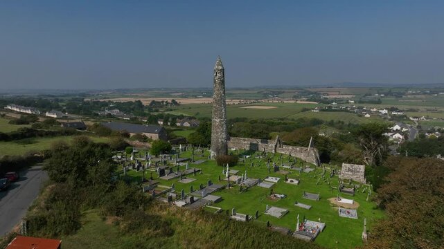 St. Declan's Monastery, Ardmore, County Waterford, Ireland, September 2024. Drone pushes towards the Round Tower and 12th century graveyard with panoramic rural countryside stretching to the horizon.