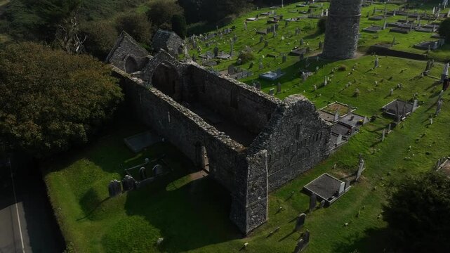 St. Declan's Monastery, Ardmore, County Waterford, Ireland, September 2024. Drone orbits counter clockwise and ascends above trees showcasing the broken stone ruin of the 12th century Cathedral.