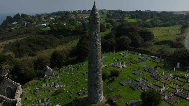 St. Declan's Monastery, Ardmore, County Waterford, Ireland, September 2024. Drone orbits counter clockwise ascending around the Round Tower and cemetery with ocean views stretching to the horizon.