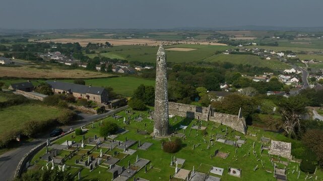 St. Declan's Monastery, Ardmore, County Waterford, Ireland, September 2024. Drone orbits clockwise above the graveyard and Cathedral ruins as blue ocean waves crash against the beach in the distance.