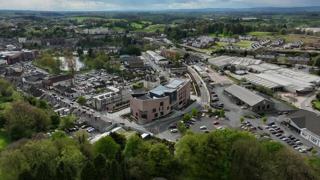 Peace Campus, County Monaghan, Ireland, April 2024. Drone orbits counter clockwise while ascending above the Monaghan County Museum with the town and Patena Lake in the background under a cloudy sky.