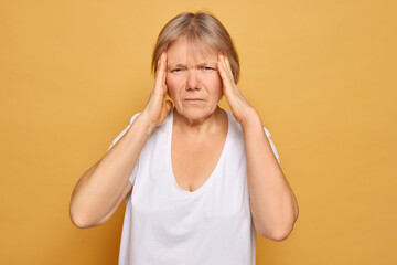 A middle-aged woman experiencing stress or headache against a solid yellow background, captured in a moment of discomfort and concern during the daytime