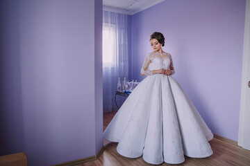 Fototapeta premium A woman in a white dress stands in front of a purple wall. She is wearing a long white gown and is posing for a picture