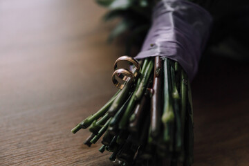 A bouquet of green stems with two gold wedding rings on top. The rings are placed in the middle of...