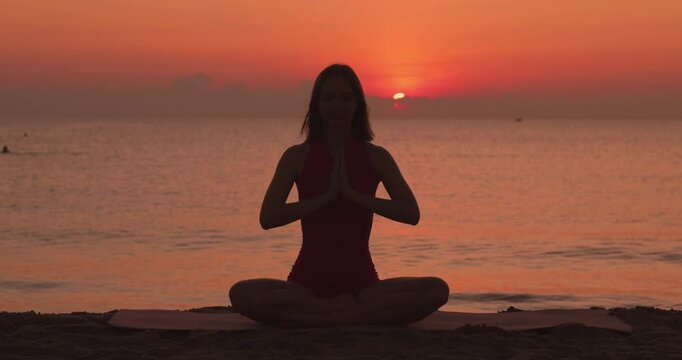 A serene silhouette of a woman practicing lotus pose with hands in prayer mudra on the beach during sunrise. This peaceful image is ideal for promoting mindfulness, wellness, and yoga, capturing the