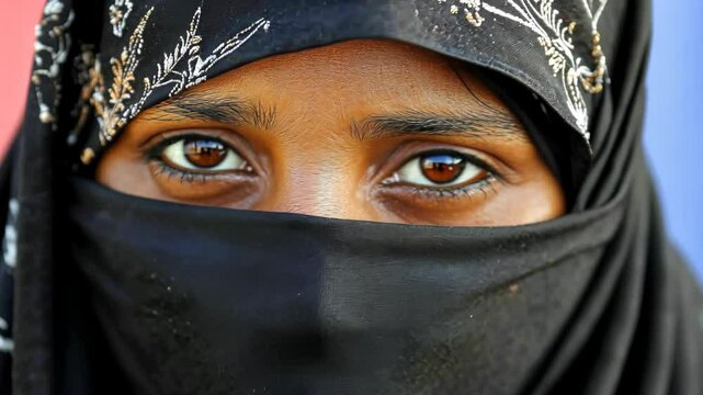 A woman wearing a black headscarf looks directly at the camera
