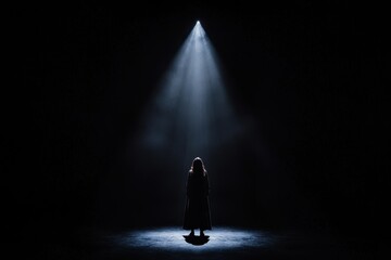 A solitary figure stands in a spotlight amidst darkness, evoking a sense of isolation and dramatic tension.