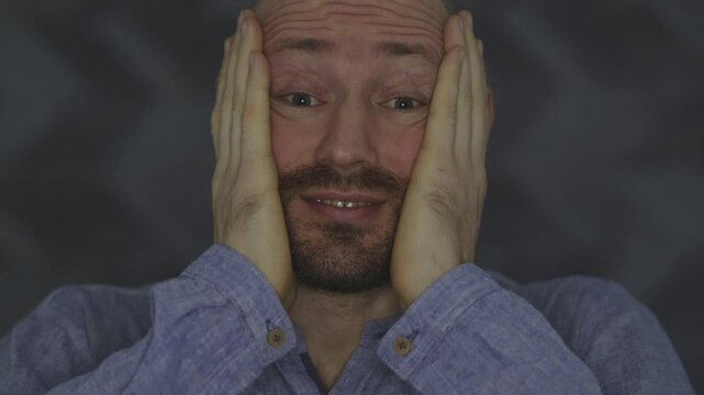 Portrait of a man with a small beard and a blue shirt, he raises his hands to his head, surprise and exasperation