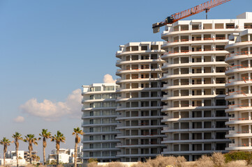 Modern beachfront construction with a crane overlooking palm trees at midday near coastal apartments