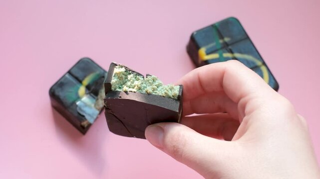 Female hand holding broken piece of Dubai chocolate on pink background top view.