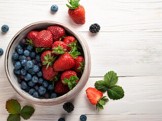 Taz&oacute;n de fresas y ar&aacute;ndanos frescos sobre fondo de madera clara