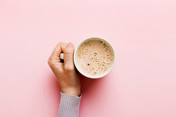 Minimalistic style woman hand holding a cup of coffee on Colored background. Flat lay, top view cappuccino cup. Empty place for text, copy space. Coffee addiction. Top view, flat lay