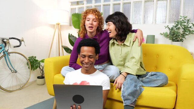 Lgtb multi-ethnic flatmates using laptop sitting on the sofa