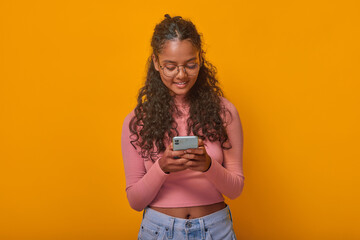 Cheerful young Indian woman with curly hair immersed in her smartphone, showcasing a relaxed vibe...