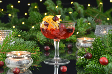 New Year's red drink in a glass with a stem decorated with lights, burning cute candles and Christmas twigs.