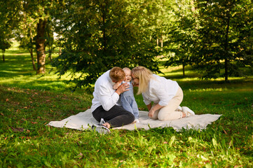 Mom and dad kiss baby, tickle him, showing love to him. Family enjoying spending time together in...