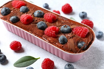 Delicious tiramisu cake with berries on table