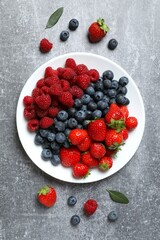 Different fresh ripe berries in bowl on the table, top view