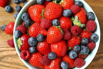 Different fresh ripe berries in bowl on the table, top view