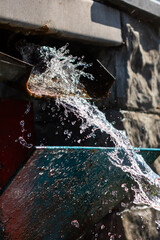Water is vigorously splashing out of a rusty and old pipe