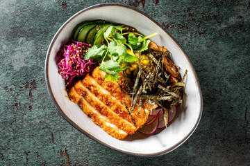 A bowl of grilled chicken, sliced cucumbers, red cabbage, herbs, radishes, and seaweed on a textured grey surface. Perfect for healthy eating, food blogs, or culinary websites