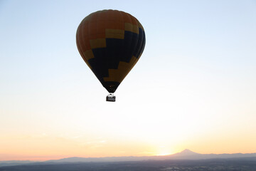 Large multi-colored Hot Air balloon flying in the blue sky above a sunrise mountains