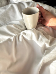Hand holding a white glasses cup at the bedding 