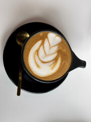 Black glasses cup of hot coffee latte on a black plate and gold spoon on the white background. Top view