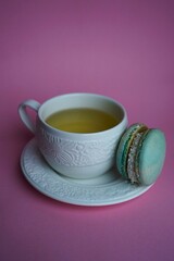 tea in a porcelain white mug with a saucer and macaroon cookies on a pink background