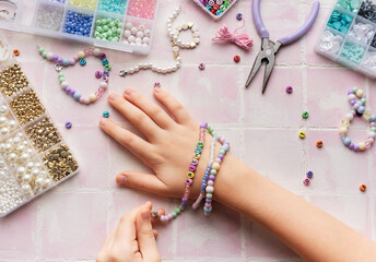 Child making beaded bracelets at home on pink tiled table