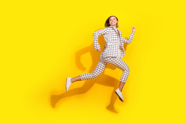 Full length photo of lovely young lady running turn around look empty space dressed white plaid garment isolated on yellow color background