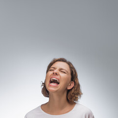 A woman in a white t-shirt yells in frustration and anguish, her face showing intense emotion...