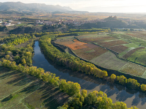 An aerial view of a lush riverbend embraces a quaint historic town, with vibrant fall colors in surrounding fields, highlighting nature's beauty and history's charm in La Rioja Spain