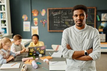 Portrait of confident African American male teacher smiling at camera posing with arms crossed in...