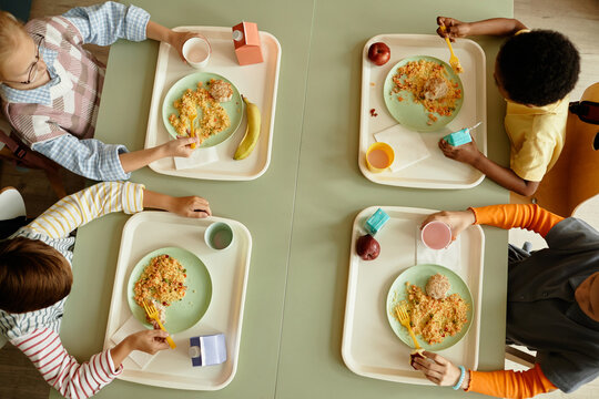 Top view of primary school children sitting together at large table enjoying eating healthy lunch in cafeteria