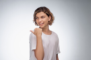 A smiling woman in a white t-shirt points backwards against a gray background. This high-quality image is perfect for concepts of direction, guidance, and positivity, ideal for various promotional and