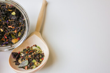 Large-grain tea with the addition of pieces of fruit and berries lies on a wooden spoon, next to it...