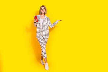 Confident young woman in stylish suit with phone against a bright yellow background, showcasing fashion and professional charisma