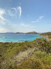  Idyllic Sardinian coastline with turquoise waters, lush vegetation, and distant sailing boats...