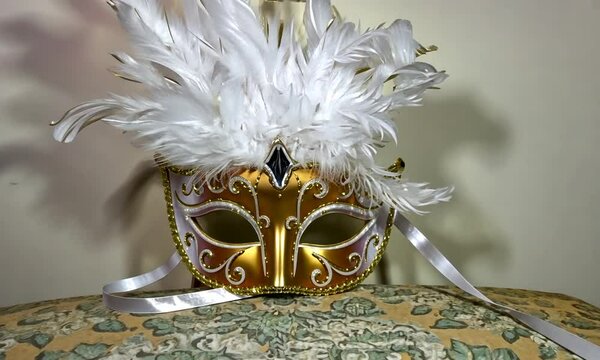 Zoom sur un masque de carnaval blanc et or, loup dor&eacute; orn&eacute; de plumes blanches &eacute;l&eacute;gantes, ambiance festive et myst&eacute;rieuse pour carnaval de Venise