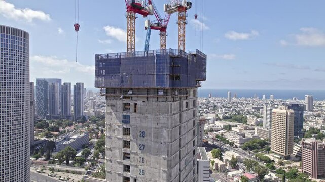 drone shot of a tall building under construction next to azrieli towers in tel aviv