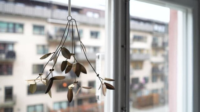Metal mistletoe hanging ornament in window facing white apartment building