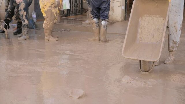 People transporting mud in wheelbarrows and unloading it on a street devastated by DANA flooding in Algemes&iacute;, Valencia