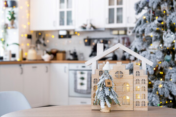 Key on Christmas tree and tiny house on cozy home with Christmas decor on table of festive white kitchen. Gift for New Year. Insurance, moving to new house, mortgage, rent and purchase real estate