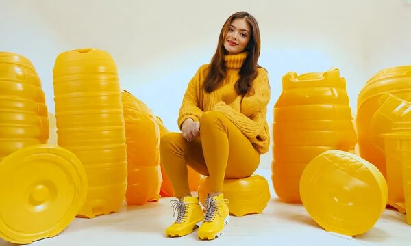 young woman sitting in winter yellow clothes and skates on big yellow plastic maccarons